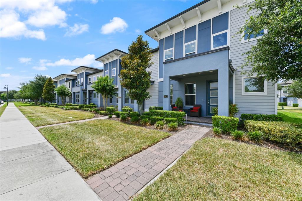 A row of modern blue and grey townhouses with paved walkways and manicured lawns — 7043 CARRICKBEND LANE, ORLANDO, FL