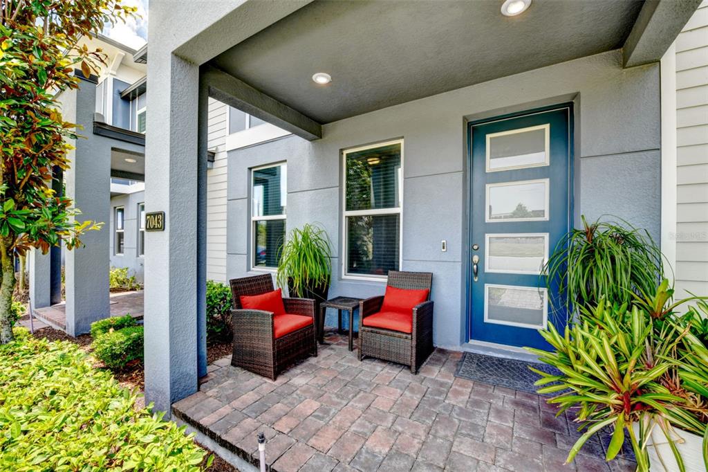 A covered front porch features a blue door, two wicker chairs, and a brick floor — 7043 CARRICKBEND LANE, ORLANDO, FL