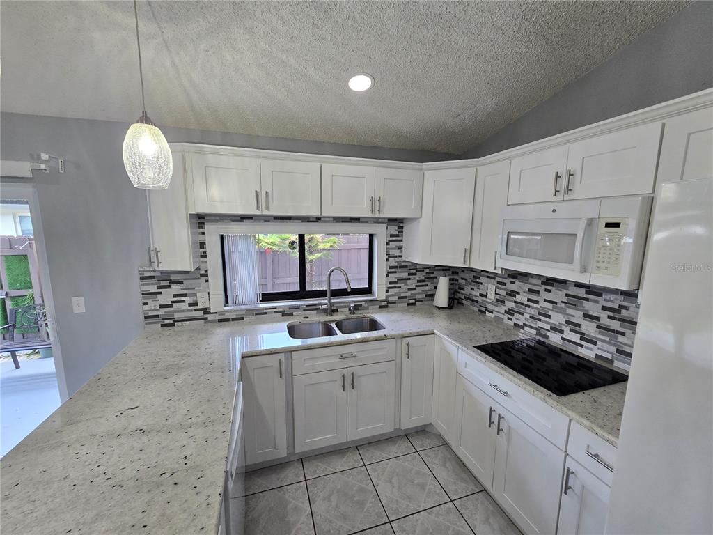A kitchen features white cabinets, granite countertops, a tiled backsplash, and a double sink — 5401 HOPEDALE DRIVE, TAMPA, FL