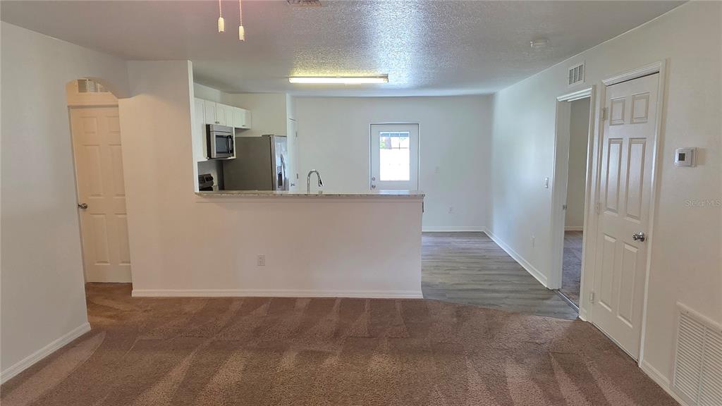A living room with carpeted flooring opens to a kitchen with a breakfast bar — 2135 19TH AVENUE SW, VERO BEACH, FL