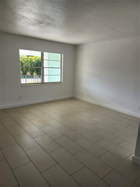 An empty room with white walls, beige tile flooring, and a window overlooking greenery — 2921 VASCO STREET UNIT A, PUNTA GORDA, FL