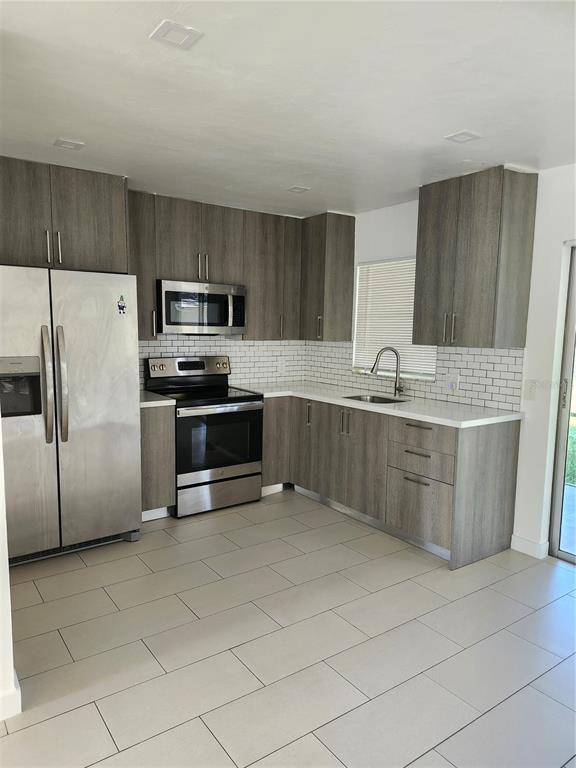 A modern kitchen features gray wood-grain cabinets, stainless steel appliances, and white subway tile backsplashes — 2921 VASCO STREET UNIT A, PUNTA GORDA, FL