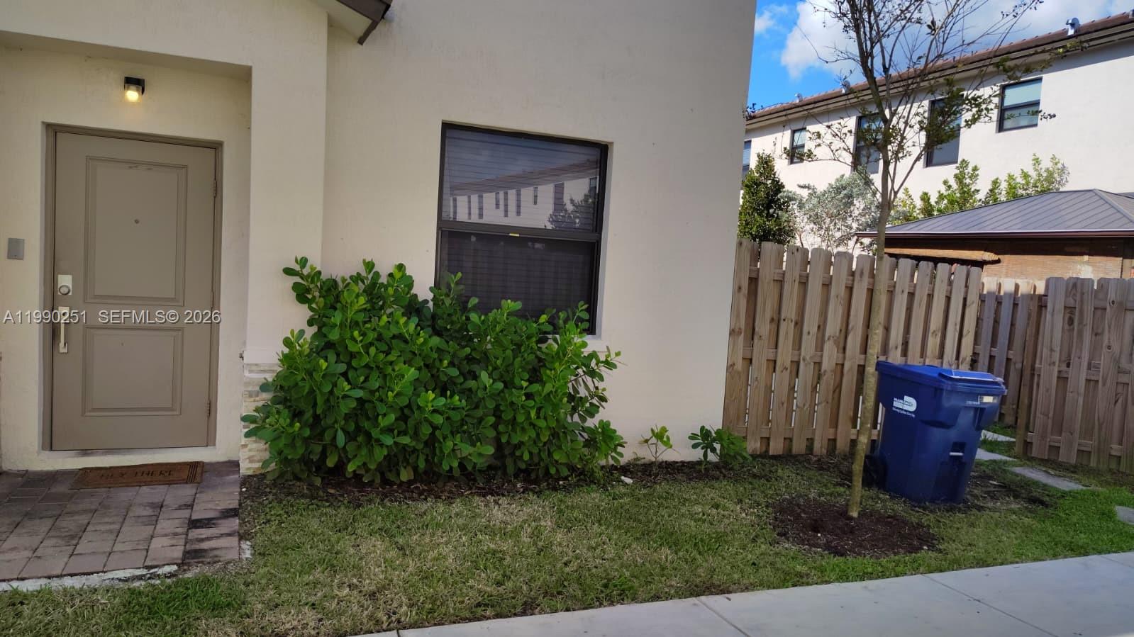 The exterior of a house features a tan door, a window, landscaping, and a trash bin — 23074 SW 128th Pl, Goulds FL 33170, GOULDS, FL