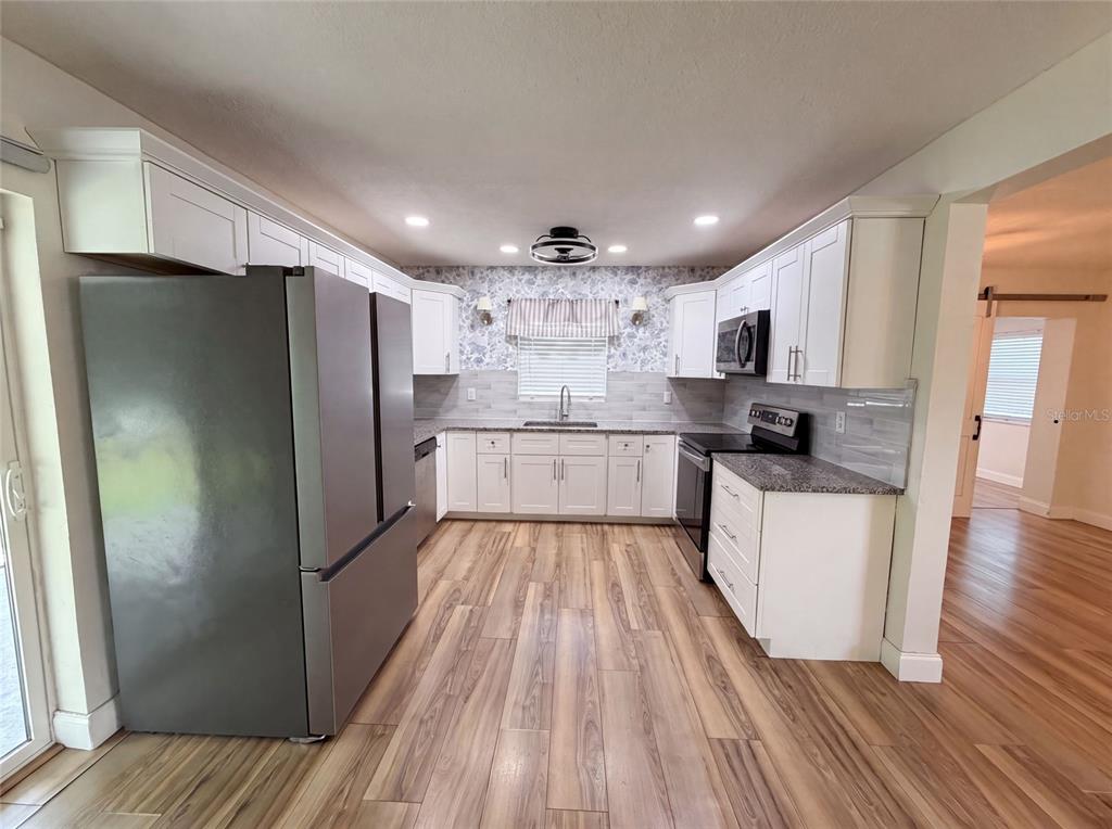 A kitchen features white cabinets, stainless steel appliances, gray countertops, and wood-look flooring — 2242 E DANA DRIVE, DELTONA, FL
