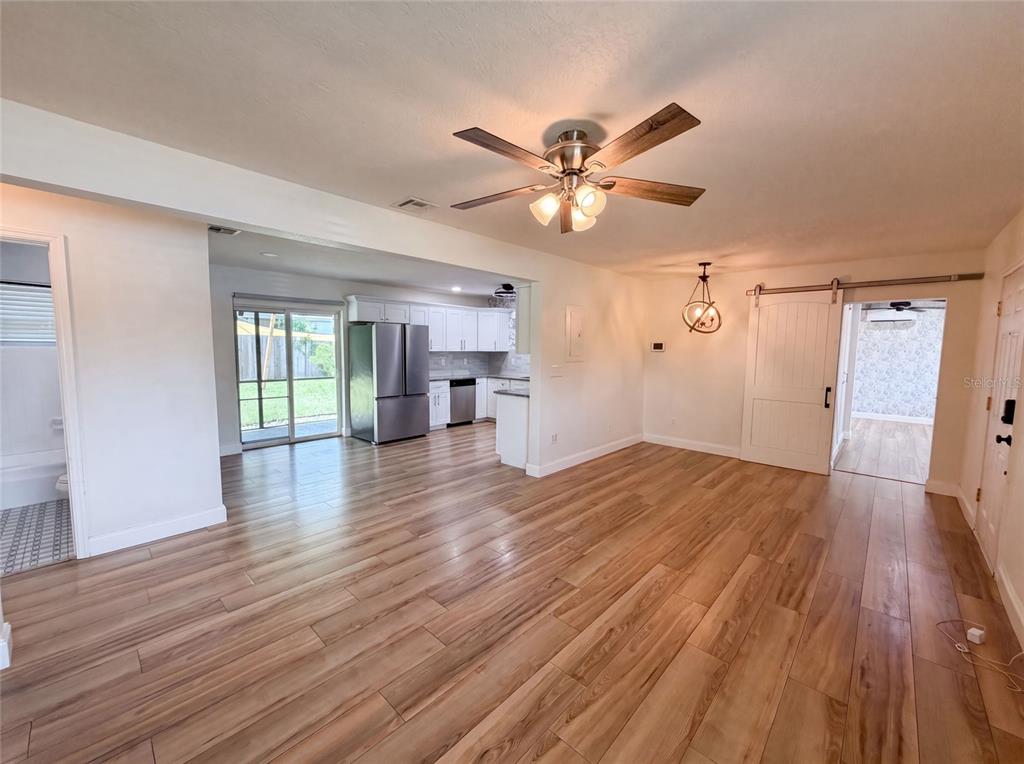 An open-concept living area with wood-look flooring, a ceiling fan, and a kitchen in back — 2242 E DANA DRIVE, DELTONA, FL