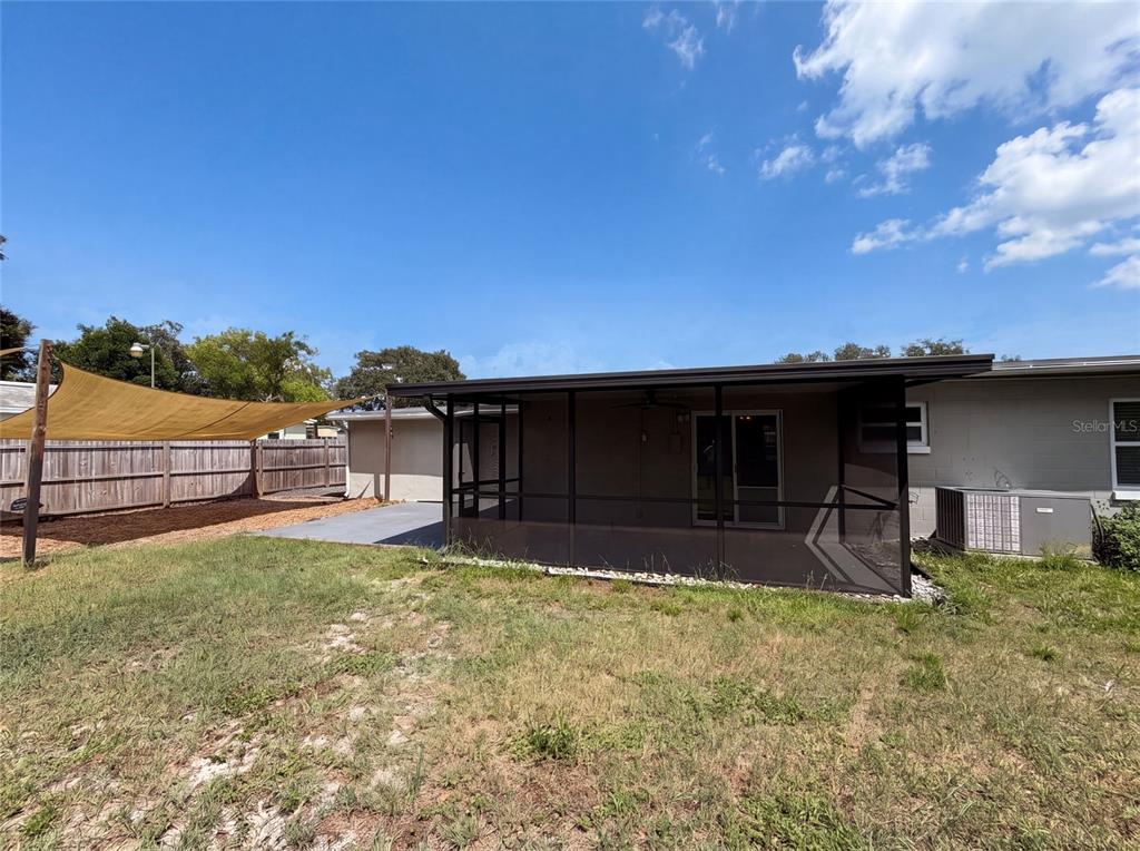 A backyard view shows a screened-in patio, a tan shade sail, and a wooden fence — 2242 E DANA DRIVE, DELTONA, FL