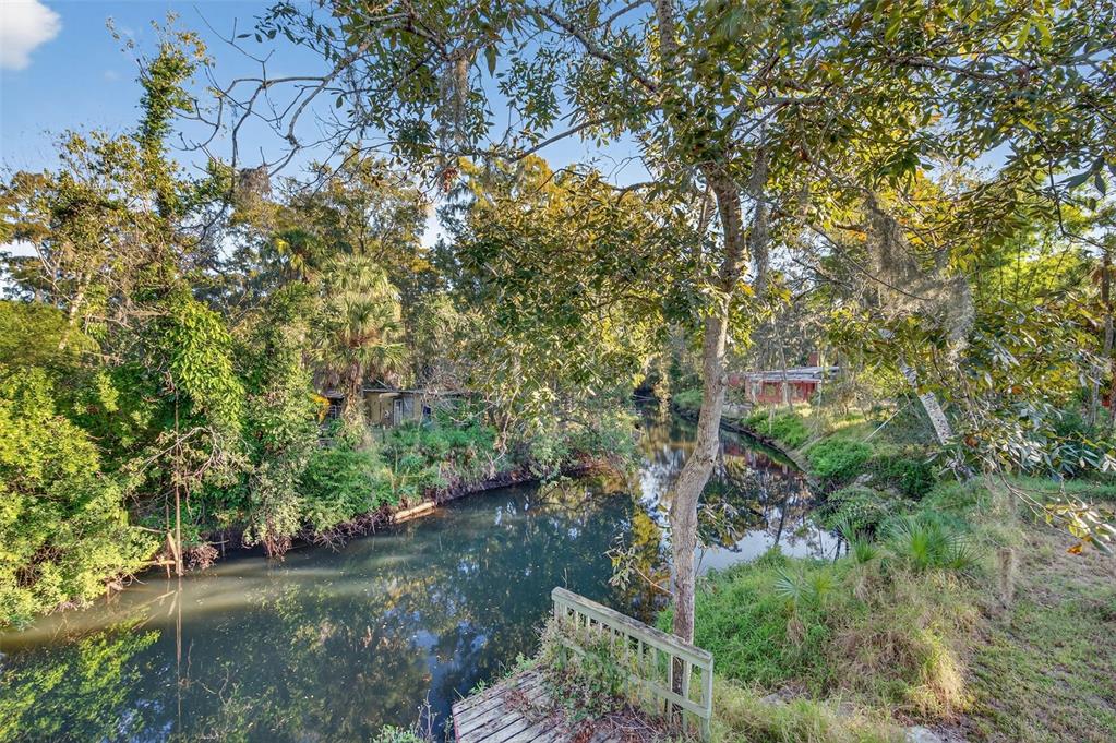 A view of a narrow, tree-lined canal with a small wooden dock in the foreground — 6345 LOST TRAIL, HOLIDAY, FL