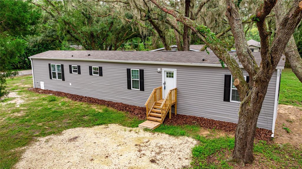 A gray manufactured home with a wooden staircase sits on a partially cleared wooded lot — 5682 NW 53RD STREET, OCALA, FL