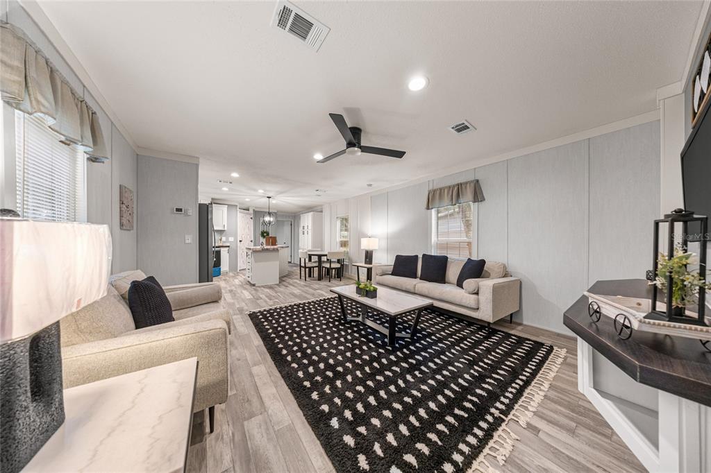 A living room with light wood-look flooring, a black patterned rug, and an open kitchen — 5682 NW 53RD STREET, OCALA, FL