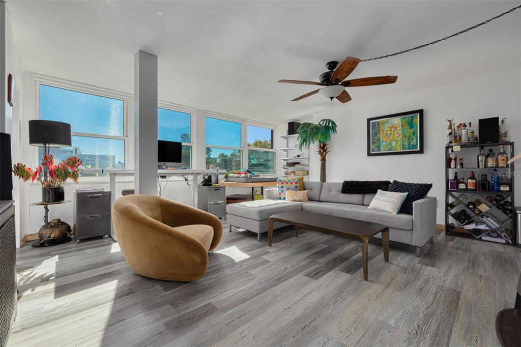 A living room features gray wood-look flooring, a sectional sofa, a swivel chair, and large windows — 841 4TH AVENUE N UNIT 38, ST PETERSBURG, FL