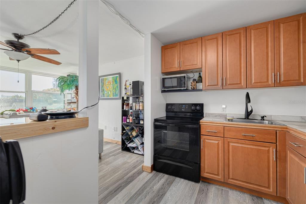 A kitchen features wood cabinets, a black stove, and a microwave next to a living area — 841 4TH AVENUE N UNIT 38, ST PETERSBURG, FL
