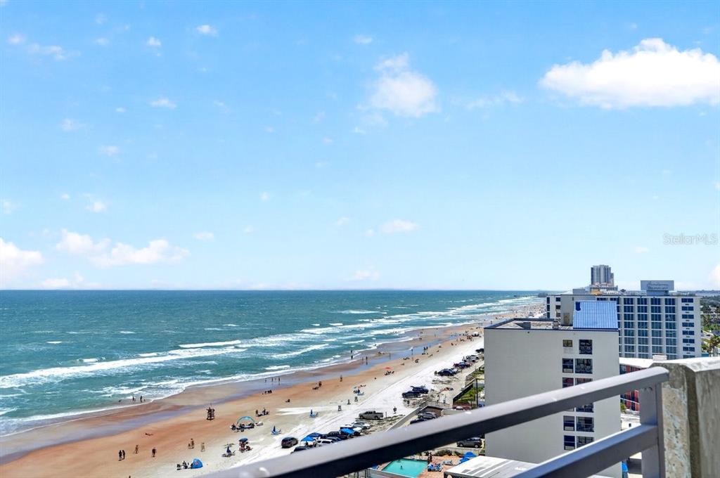 A bedroom features a bed with green accents, dark curtains, and a view of water — 1420 N ATLANTIC AVENUE UNIT 1104, DAYTONA BEACH, FL