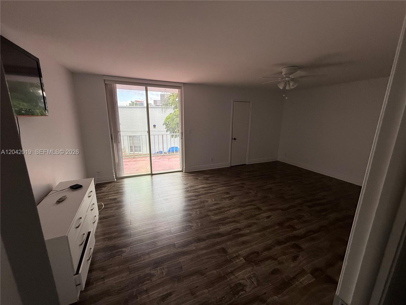 A bright living room features wood-look flooring, a white dresser, and a sliding glass door — 2606 NE 10 ST # 2606, Hallandale Beach FL 33009, HALLANDALE BEACH, FL