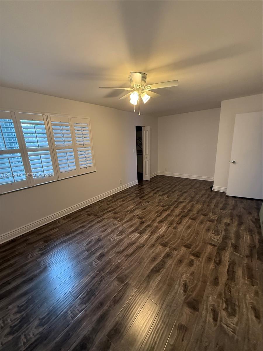 An empty bedroom features dark wood-look flooring, white walls, plantation shutters, and a ceiling fan — 2606 NE 10 ST # 2606, Hallandale Beach FL 33009, HALLANDALE BEACH, FL