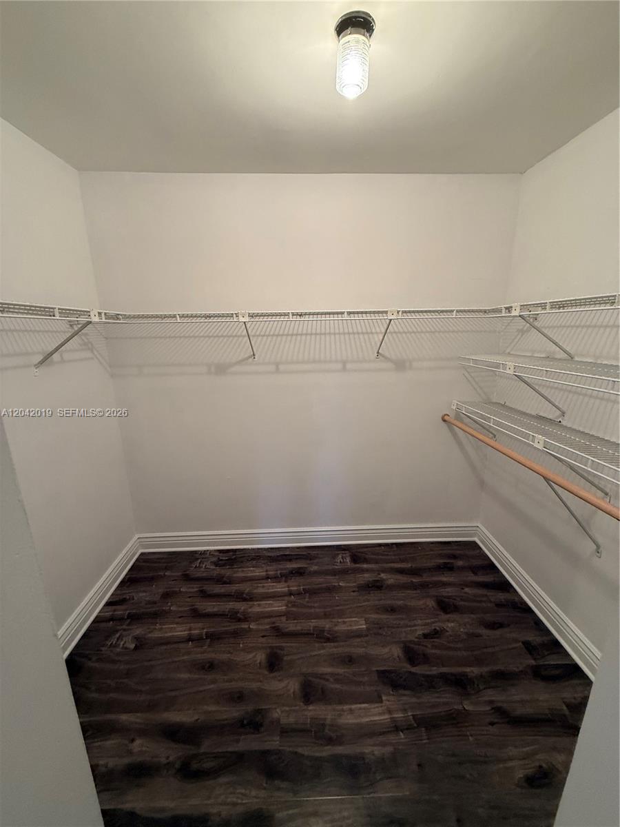 A walk-in closet features white wire shelving, a wooden hanging rod, and dark wood flooring — 2606 NE 10 ST # 2606, Hallandale Beach FL 33009, HALLANDALE BEACH, FL