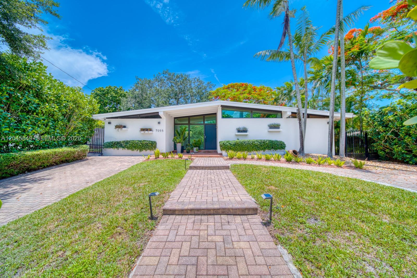 A single-story white house with a brick walkway and palm trees under a blue sky — 7055 SW 84th Ave, Miami FL 33143, MIAMI, FL