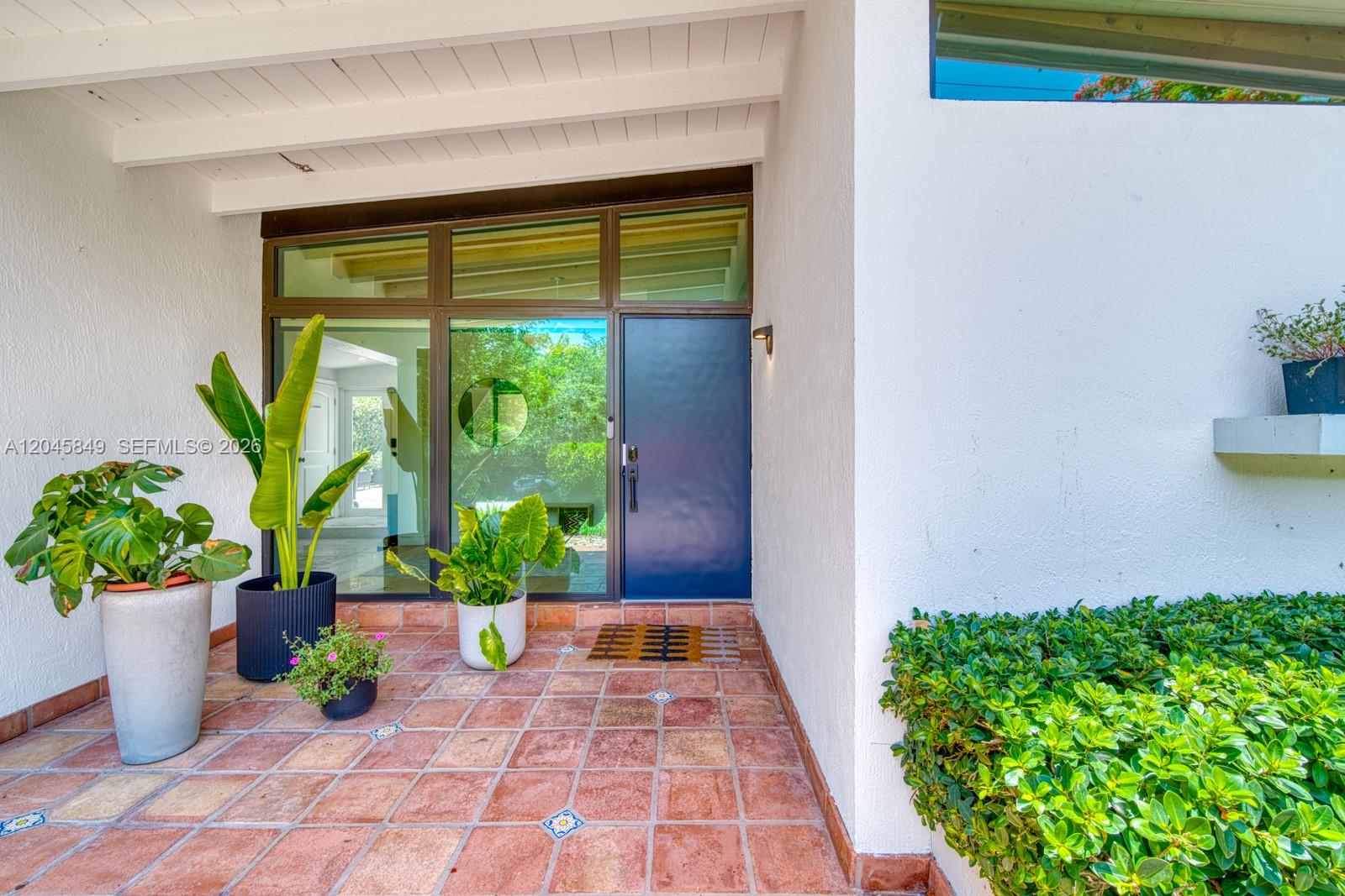 A front entryway features a blue door, glass panels, potted plants, and terracotta tile flooring — 7055 SW 84th Ave, Miami FL 33143, MIAMI, FL