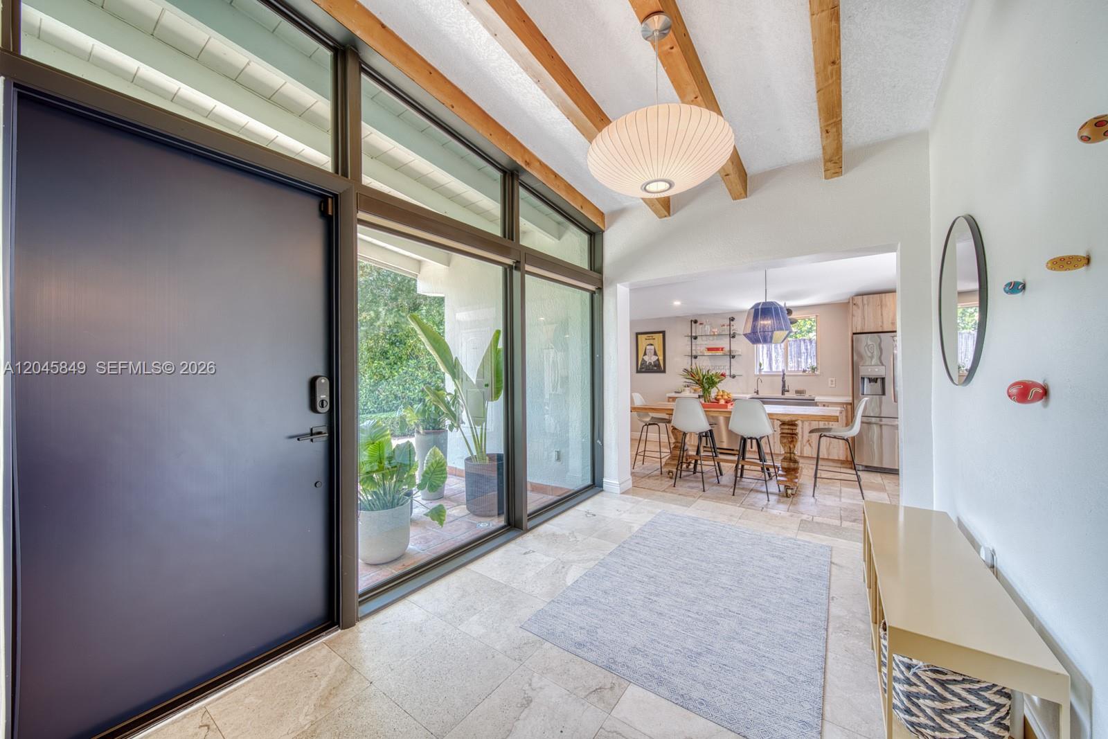 A bright entryway features a dark door, floor-to-ceiling windows, exposed wood beams, and tile flooring — 7055 SW 84th Ave, Miami FL 33143, MIAMI, FL