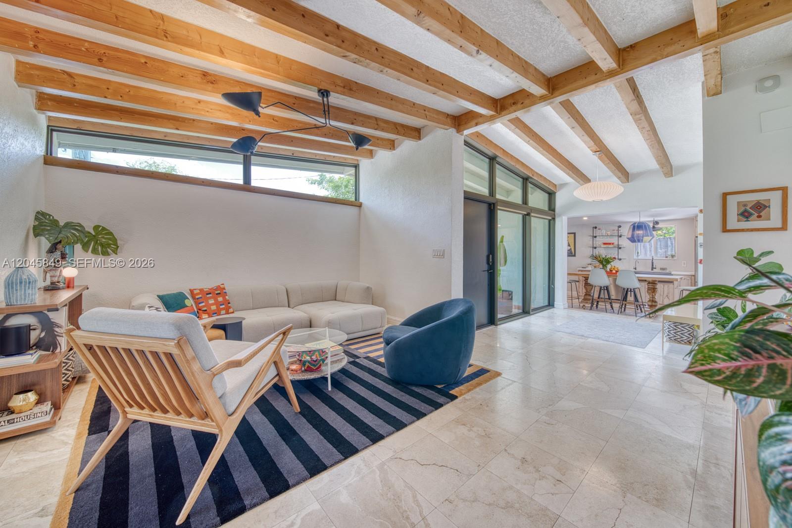 A living room features exposed wood ceiling beams, a striped rug, and a kitchen beyond — 7055 SW 84th Ave, Miami FL 33143, MIAMI, FL
