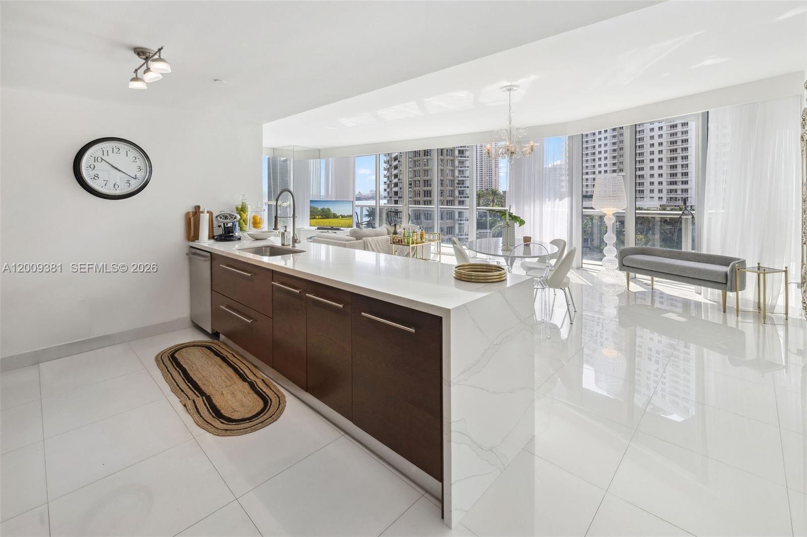 A modern kitchen with dark wood cabinets and a white waterfall island overlooks a city — 465 Brickell Ave # 701, Miami FL 33131, MIAMI, FL