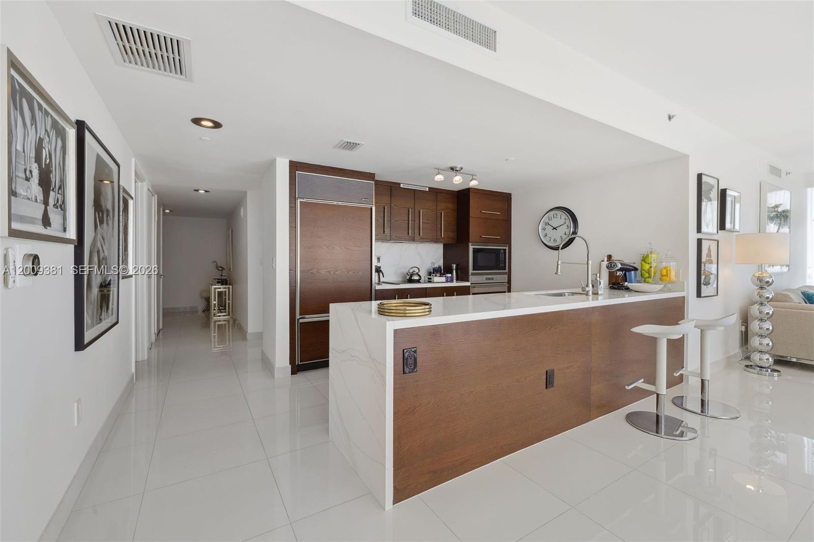 A modern kitchen features a white quartz island with wood paneling and white tile floors — 465 Brickell Ave # 701, Miami FL 33131, MIAMI, FL
