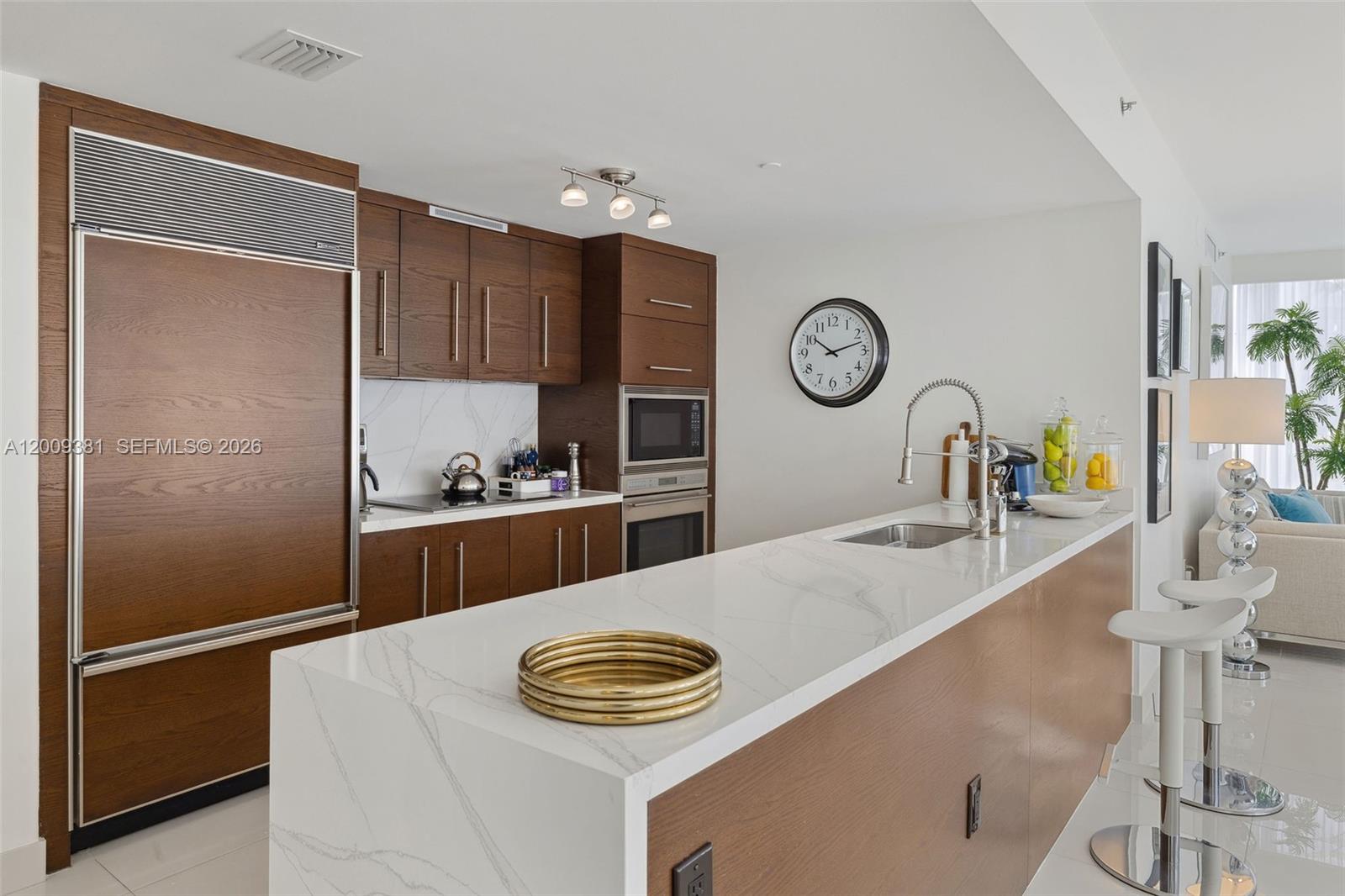 A modern kitchen features wood cabinets, white marble countertops, and a central island with seating — 465 Brickell Ave # 701, Miami FL 33131, MIAMI, FL