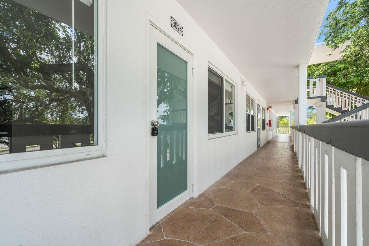 An outdoor walkway with stone-patterned flooring leads past a glass door and windows — 3024 Oakridge D # 3024, Deerfield Beach FL 33442, DEERFIELD BEACH, FL