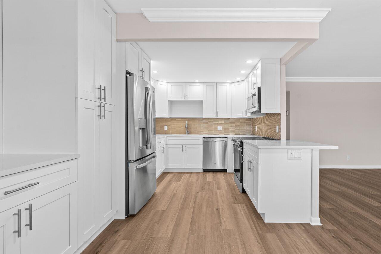 A modern white kitchen features stainless steel appliances, light wood flooring, and a peninsula island — 3024 Oakridge D # 3024, Deerfield Beach FL 33442, DEERFIELD BEACH, FL
