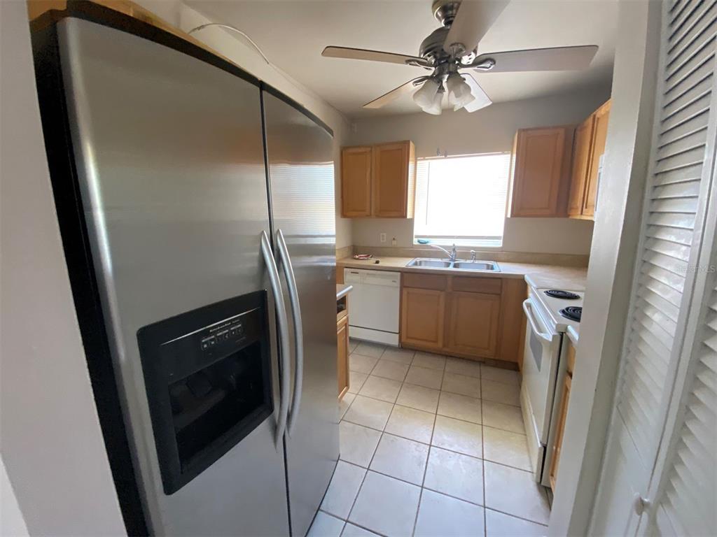 A kitchen features stainless steel appliances, wood cabinets, tile flooring, and a ceiling fan — 22017 BEVERLY AVENUE, PORT CHARLOTTE, FL