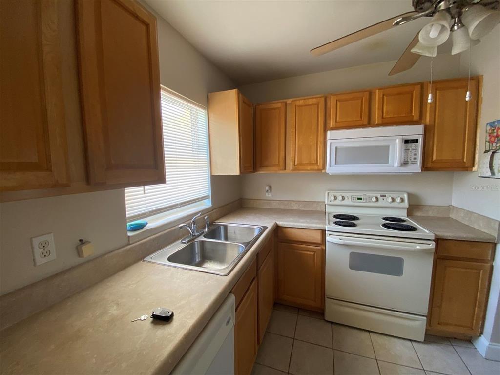 A kitchen features light wood cabinets, white appliances, a double sink, and beige countertops — 22017 BEVERLY AVENUE, PORT CHARLOTTE, FL
