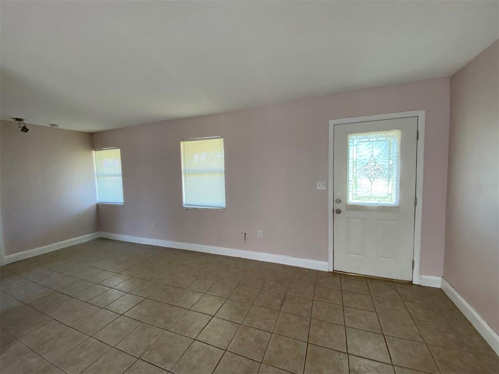 An empty room with light pink walls, tan tile flooring, two windows, and a white door — 22017 BEVERLY AVENUE, PORT CHARLOTTE, FL