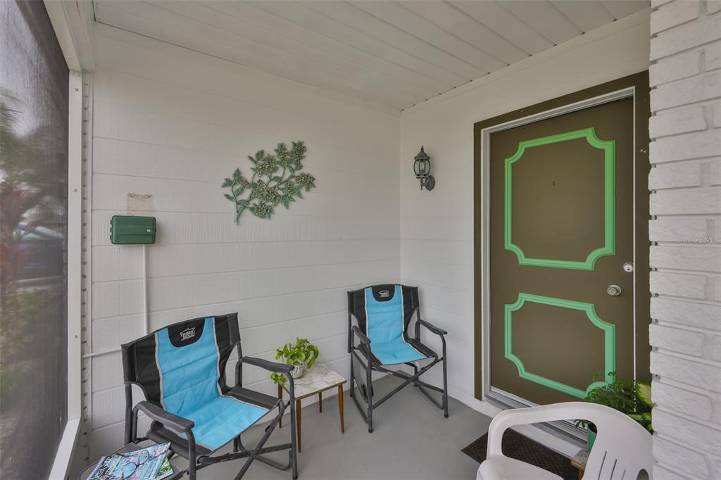 A screened-in porch features two folding chairs, a small table, and a brown front door — 1520 DANBURY DRIVE, SUN CITY CENTER, FL