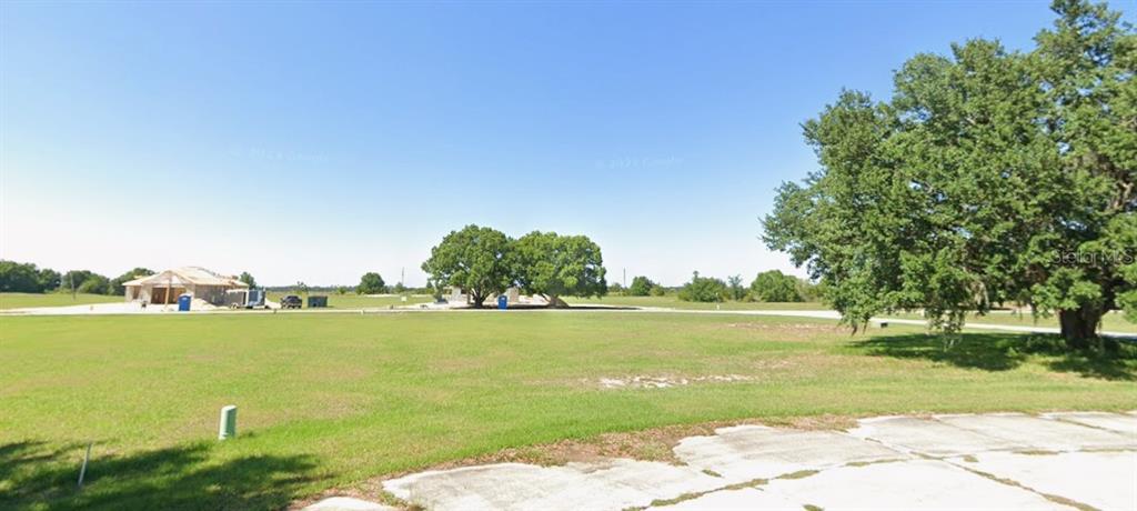 A large, grassy vacant lot features a house under construction and several mature oak trees — 1209 GOLF COURT, SEBRING, FL