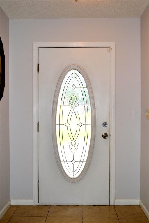 A white front door with an oval glass insert is centered in a tiled entryway — 6496 TOLEDO ROAD, SPRING HILL, FL