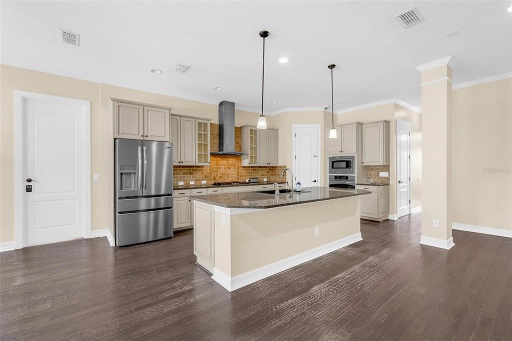 A kitchen features light-colored cabinets, stainless steel appliances, a granite island, and dark wood floors — 7231 SANGALLA DRIVE, WINDERMERE, FL