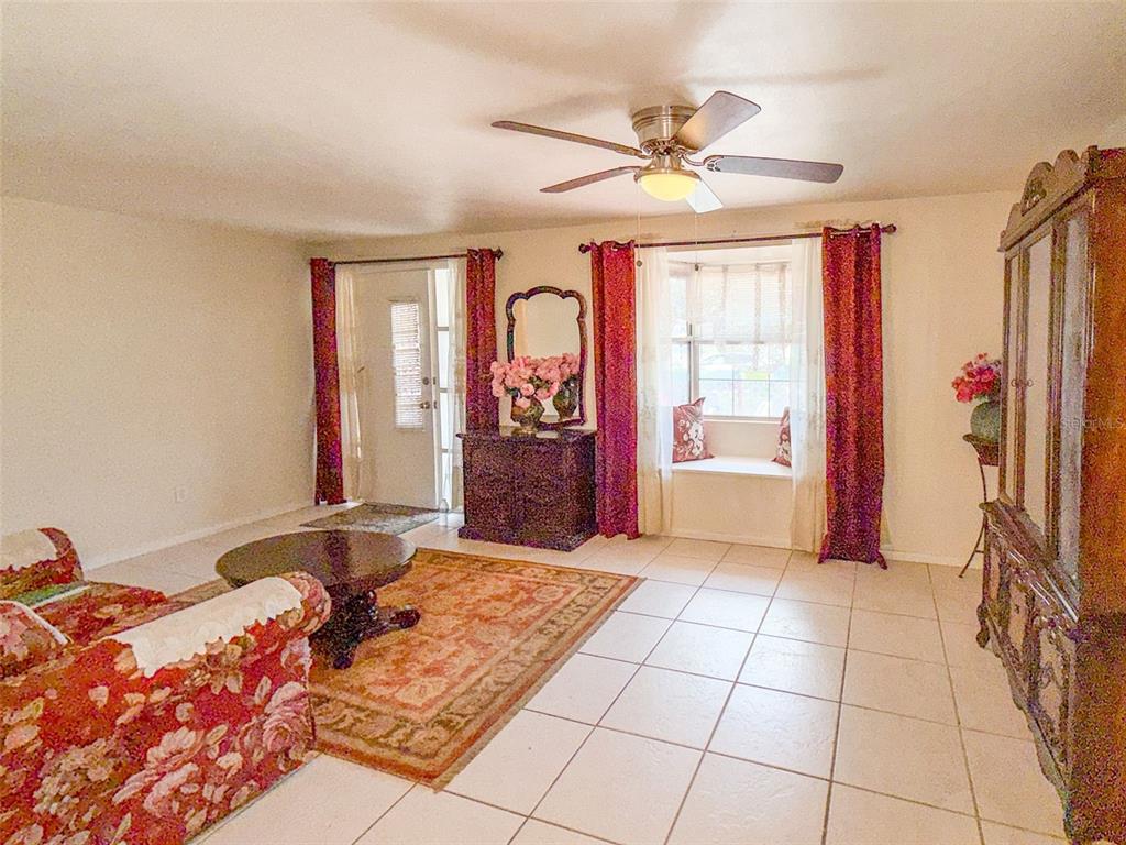 A living room features tile flooring, a floral sofa, a round coffee table, and curtains — 4737 LONGWOOD AVENUE, HOLIDAY, FL