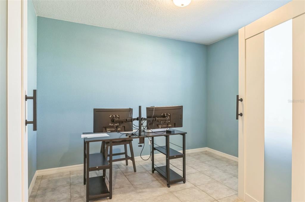 A small home office with light blue walls, tile flooring, and a dual-monitor desk setup — 1262 CITRUS LANDINGS BOULEVARD, DAVENPORT, FL