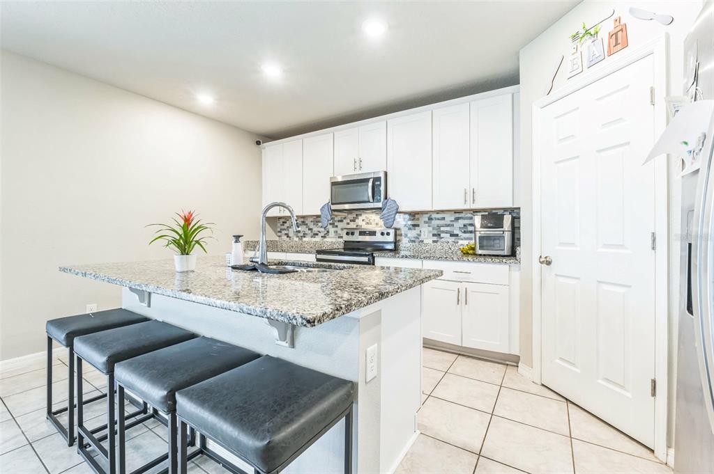 A kitchen features white cabinetry, granite countertops, a center island with bar seating, and tile flooring — 1262 CITRUS LANDINGS BOULEVARD, DAVENPORT, FL