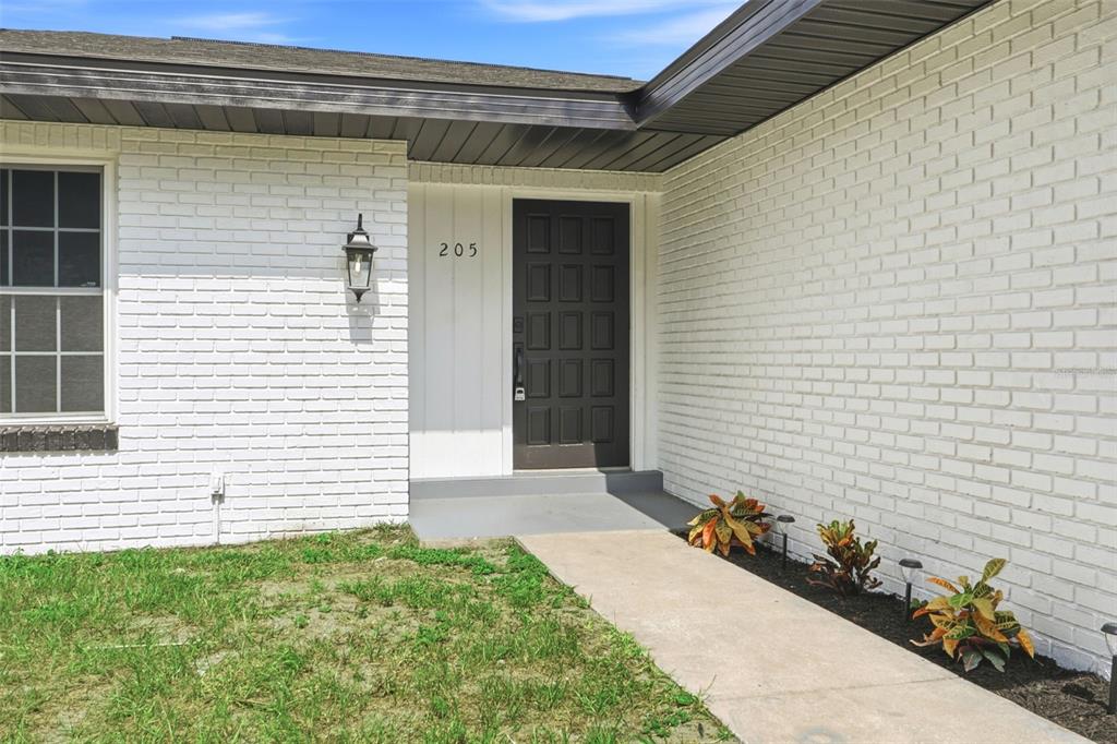 A white brick house exterior features a dark front door and a concrete walkway — 205 WHITMAN ROAD, WINTER HAVEN, FL