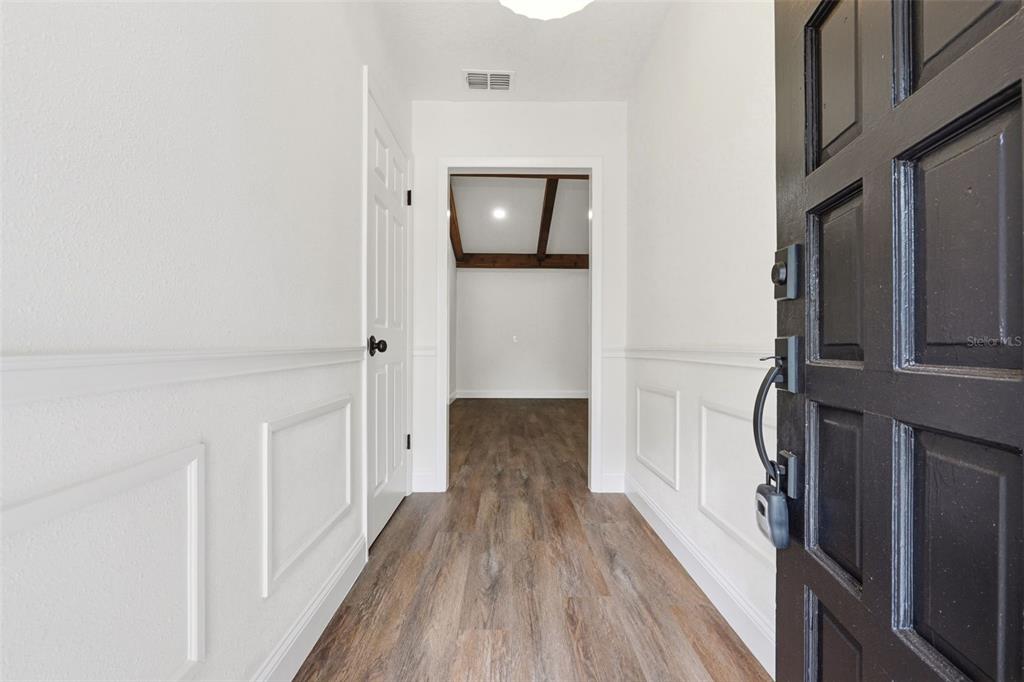 An entryway with wood-look flooring, white wainscoting, and a black door leads to another room — 205 WHITMAN ROAD, WINTER HAVEN, FL