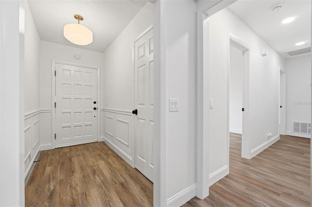 An entryway with white wainscoting, wood-look flooring, and a white front door — 205 WHITMAN ROAD, WINTER HAVEN, FL