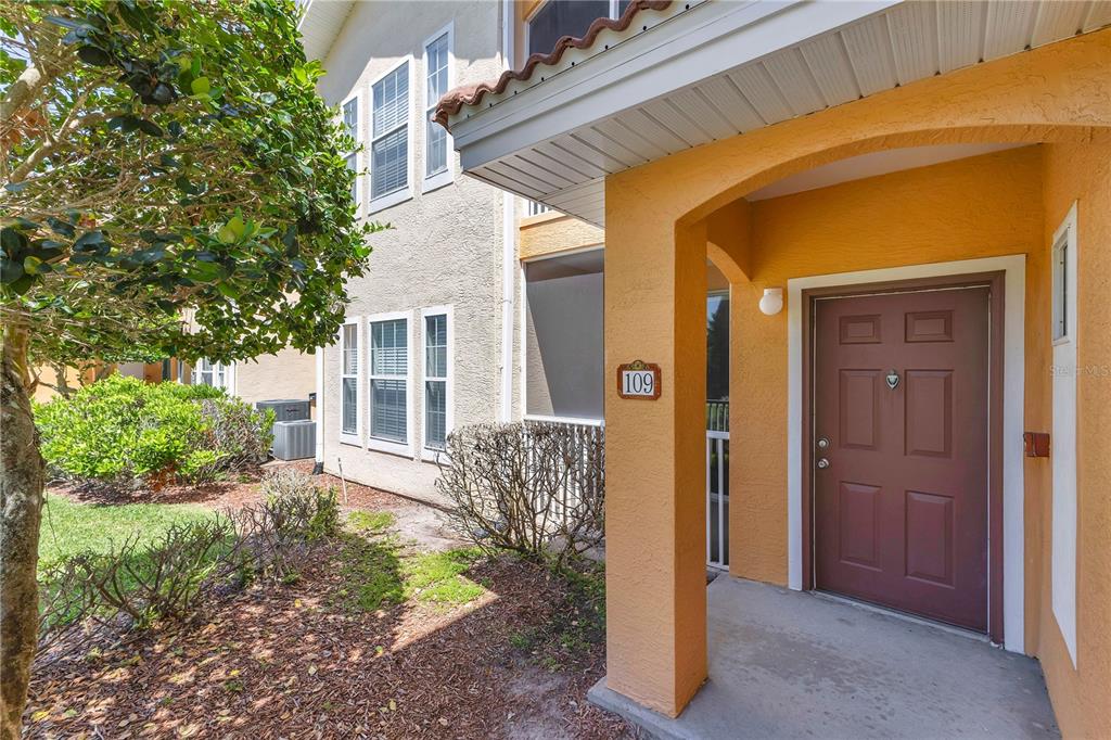 The exterior of a tan building features a covered entryway with a brown front door — 12111 POPPY FIELD LANE UNIT 109, ORLANDO, FL