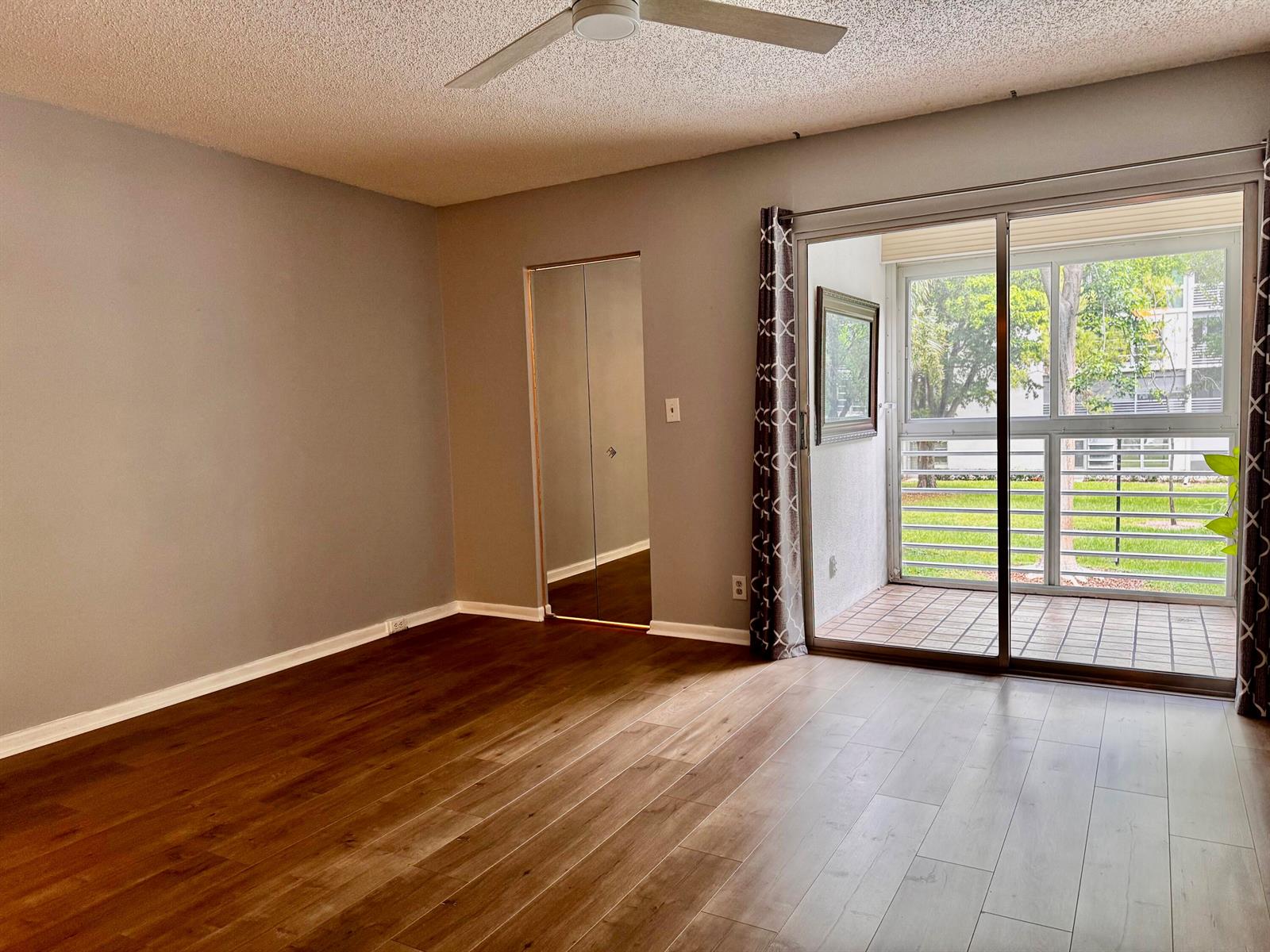 A bedroom features a white bed, light wood flooring, and a sliding glass door to a balcony — 2003 Granada Drive # J2, Coconut Creek FL 33066, COCONUT CREEK, FL
