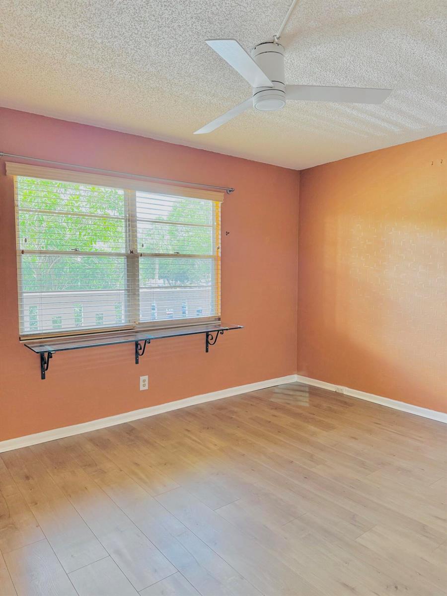 A bedroom features peach-colored walls, a gray upholstered bed, and a window with blinds — 2003 Granada Drive # J2, Coconut Creek FL 33066, COCONUT CREEK, FL