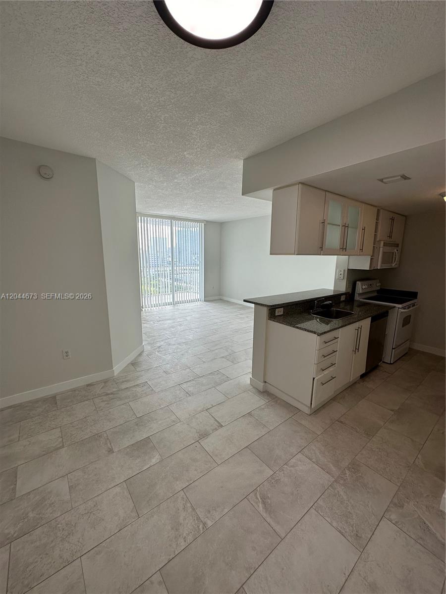 A kitchen with white cabinets and granite countertops opens into a living area with tile — 275 NE 18th St # 1406, Miami FL 33132, MIAMI, FL