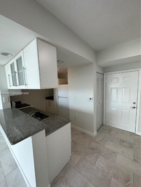A kitchen with granite countertops and white cabinets opens into a tiled entryway — 275 NE 18th St # 1406, Miami FL 33132, MIAMI, FL