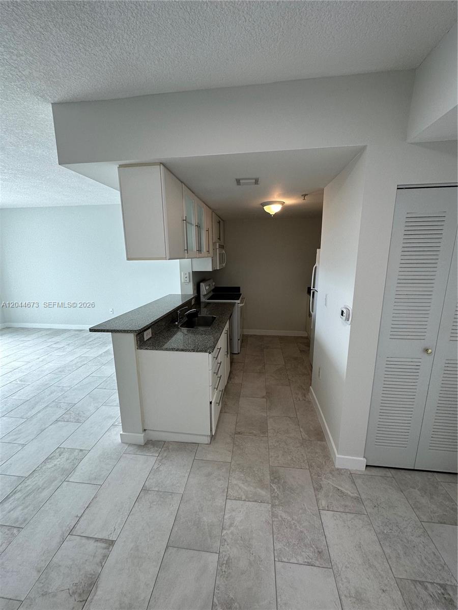 A galley-style kitchen features white cabinets, granite countertops, and light-colored tile flooring — 275 NE 18th St # 1406, Miami FL 33132, MIAMI, FL
