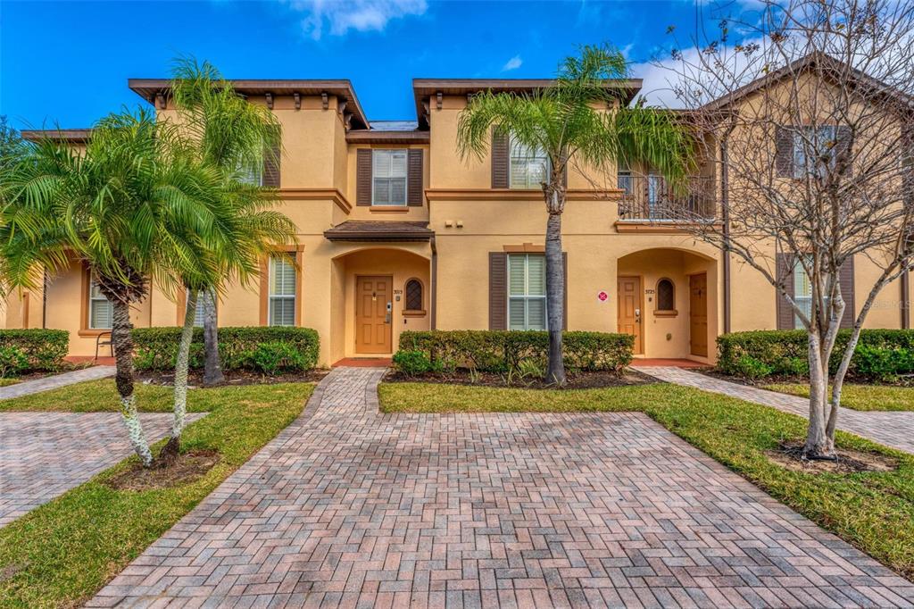 A two-story tan stucco townhouse exterior with palm trees and a brick paver walkway — 3715 CALABRIA AVENUE, DAVENPORT, FL