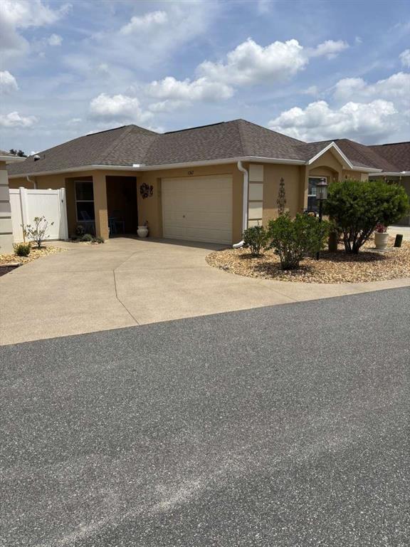 A tan single-story house with a two-car garage and a concrete driveway — 1067 CARVER COURT, THE VILLAGES, FL