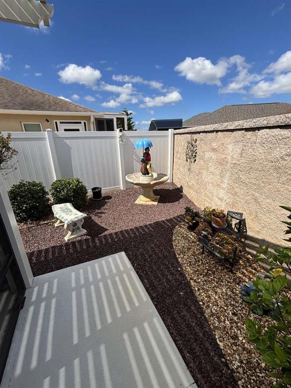 A small backyard features a stone fountain, a white fence, and a gravel ground cover — 1067 CARVER COURT, THE VILLAGES, FL